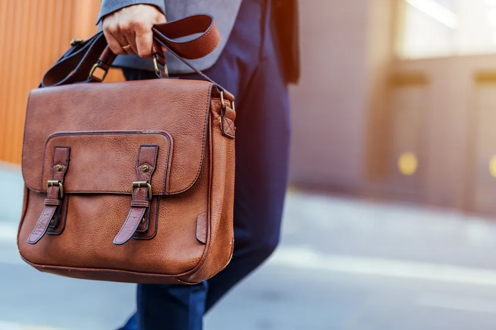 A businessman confidently carries a brown leather briefcase in a city environment. The image embodies professionalism, style, and mobility, ideal for business or travel themes.